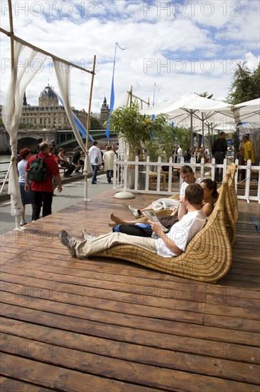 FRANCE, Ile de France, Paris, "The Paris Plage urban beach. People strolling between the River Seine and other people lying on whicker chairs along the Voie Georges Pompidou usually a busy road, now closed to traffic opposite the Ile de la Cite"