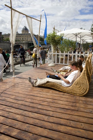 FRANCE, Ile de France, Paris, "The Paris Plage urban beach. People strolling between the River Seine and other people lying on whicker chairs along the Voie Georges Pompidou usually a busy road, now closed to traffic opposite the Ile de la Cite"