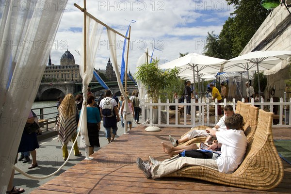 FRANCE, Ile de France, Paris, "The Paris Plage urban beach. People strolling between the River Seine and other people lying on whicker chairs along the Voie Georges Pompidou usually a busy road, now closed to traffic opposite the Ile de la Cite"