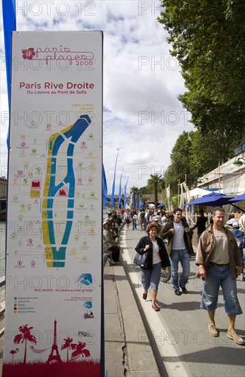 FRANCE, Ile de France, Paris, The Paris Plage urban beach. People strolling beside the River Seine along the Voie Georges Pompidou usually a busy road now closed to traffic opposite the Ile de la Cite with a map showing the attractions along the Rive Droite