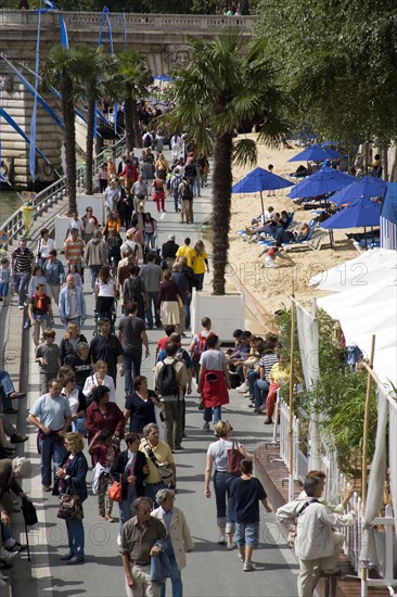 FRANCE, Ile de France, Paris, The Paris Plage urban beach. People strolling between the River Seine and people lying on sand along the Voie Georges Pompidou usually a busy road now closed to traffic opposite the Ile de la Cite