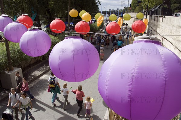 FRANCE, Ile de France, Paris, The Paris Plage urban beach. Colourful lanterns hanging above pedestrians strolling along the Voie Georges Pompidou a usually busy road closed to traffic opposite the Ile de la Cite