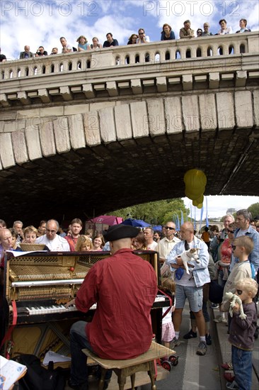 FRANCE, Ile de France, Paris, The Paris Plage urban beach. A singer playing a piano to an audience under the Pont Notre Dame on the Voie Georges Pompidou a usually busy road closed to traffic