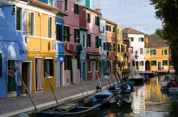 ITALY, Veneto, Venice, Colourful houses beside a canal on the lagoon island of Burano with boats moored alongside the edge of the canal