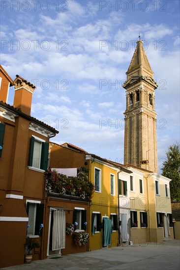 ITALY, Veneto, Venice, The leaning bell tower of the church on the lagoon island of Burano set behind colourful terraced housing