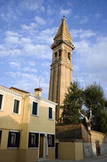 ITALY, Veneto, Venice, The leaning bell tower of the church on the lagoon island of Burano set behind colourful terraced housing