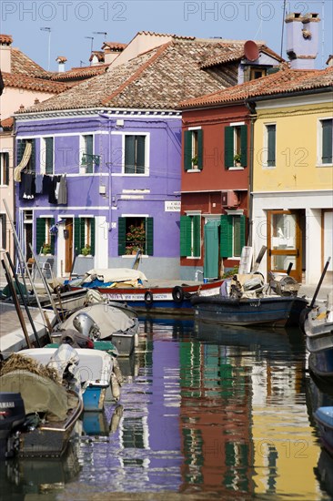 ITALY, Veneto, Venice, Colourful houses beside a canal on the lagoon island of Burano with boats moored alongside the edge of the canal.