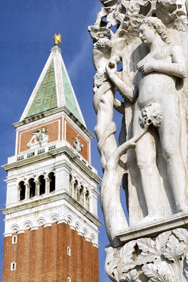 ITALY, Veneto, Venice, Stone carving of Eve and The Serpent on the corner of the Doges Palace in the Piazzetta with the Campanile tower in Saint Mark's Square beyond