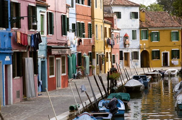 ITALY, Veneto, Venice, Colourful houses beside a canal on the lagoon island of Burano with boats moored alongside the edge of the canal.