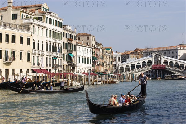 ITALY, Veneto, Venice, A Traghetto with local people on board crosses the Grand Canal and a Gondola carries tourists down river. Tourists crowd on the Rialto Bridge spanning the canal