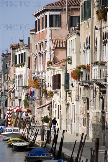 ITALY, Veneto, Venice, Colourful houses along the Fondamenta de la Sensa in Cannaregio district with boats moored along the canal and people walking along the pavement