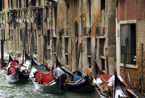 ITALY, Veneto, Venice, Gondoliers resting with their gondolas moored at the edge of the Rio Dei Barcaroli canal in San Marco district