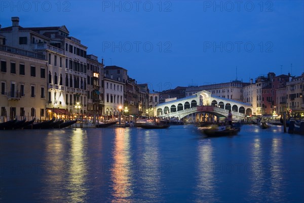ITALY, Veneto, Venice, The Rialto Bridge spanning the Grand Canal illuminated at night with the canal busy with various water transport