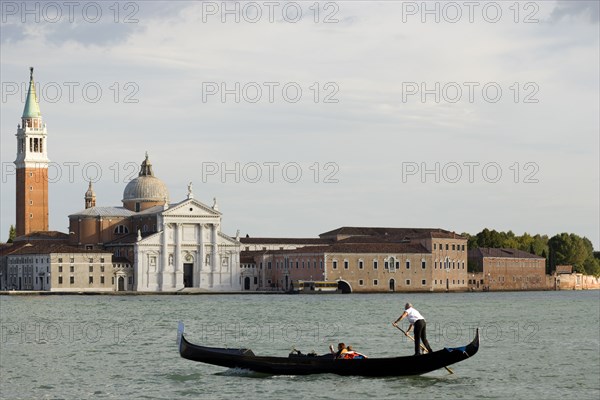 ITALY, Veneto, Venice, A gondola with tourists crosses the Basin of San Marco in front of Palladio's church of San Giorgio Maggiore on the island of the same name