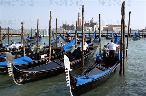 ITALY, Veneto, Venice, Gondoliers prepare gondolas in the Molo San Marco basin in front of Palladio's church of San Giorgio Maggiore on the island of the same name