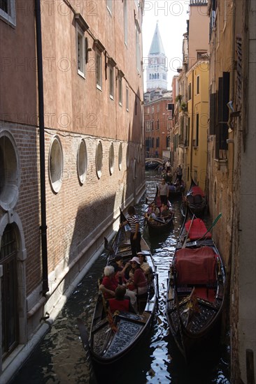 ITALY, Veneto, Venice, Gondoliers carry sightseeing tourists in gondolas along the norrow Rio di San Salvador canal with the Campanile in the distance in Piazza San Marco