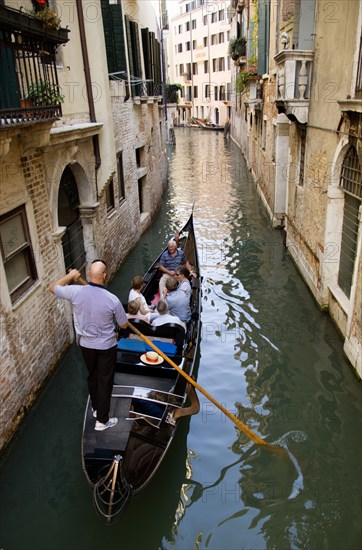 ITALY, Veneto, Venice, Gondolier carries sightseeing tourists in his gondola along a norrow canal in the San Marco disrtrict