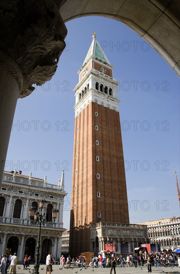 ITALY, Veneto, Venice, The Campanile in Piazza San Marco seen through an arch below the Doges Palace with tourists walking in the square