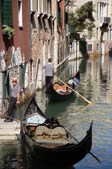 ITALY, Veneto, Venice, A Gondola with tourists passing along a canal in the San Marco district. Another gondolier waits by some steps for passengers