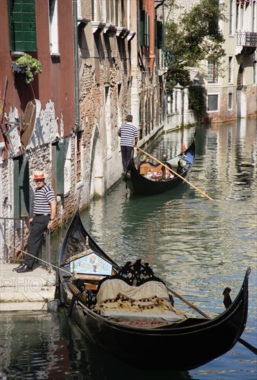 ITALY, Veneto, Venice, A Gondola with tourists passing along a canal in the San Marco district. Another gondolier waits by some steps for passengers