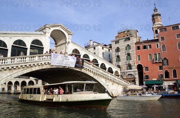 ITALY, Veneto, Venice, A vapretto passes below the Rialto Bridge with tourists viewing the canal