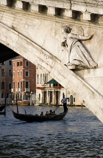 ITALY, Veneto, Venice, A gondola carrying tourists passes beneath the Rialto Bridge over the Grand Canal