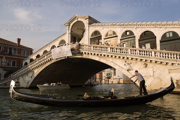 ITALY, Veneto, Venice, An empty gondola passes in front of the Rialto Bridge over the Grand Canal at sunset