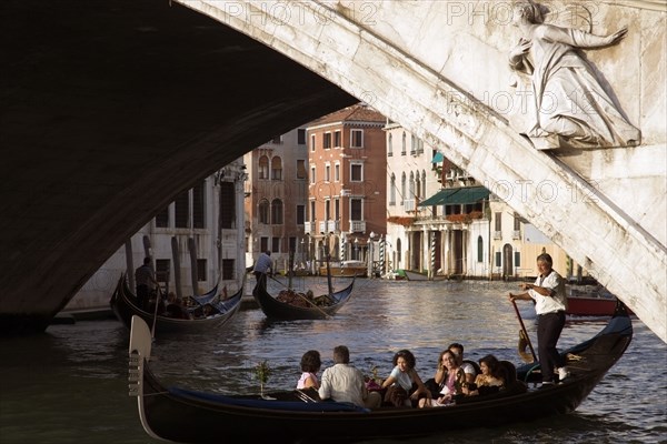 ITALY, Veneto, Venice, A gondola carrying tourists passes beneath the Rialto Bridge over the Grand Canal