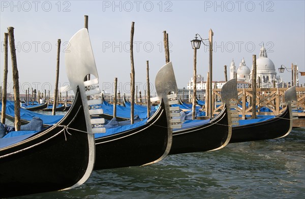 ITALY, Veneto, Venice, Ferros or bows of Gondolas moored in the Molo San Marco basin with the Baroque church of Santa Maria della Salute on the Grand Canal in the distance