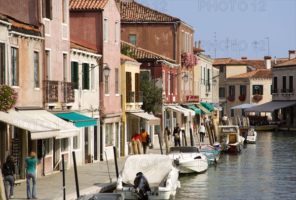 ITALY, Veneto, Venice, Tourists walking past shops along the Fondamenta dei Vetrai with boats moored on the Rio dei Vetrai canal on the lagoon island of Murano