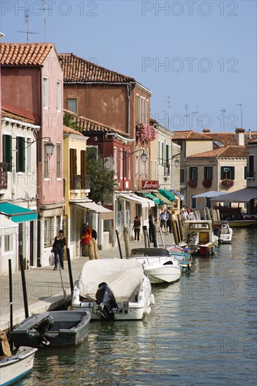 ITALY, Veneto, Venice, Tourists walking past shops along the Fondamenta dei Vetrai with boats moored on the Rio dei Vetrai canal on the lagoon island of Murano