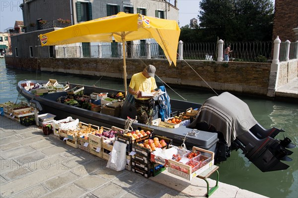 ITALY, Veneto, Venice, A fruit and vegetable vendor with his boat moored alongside the Fondamenta dei Vetrai along the Rio dei Vetrai canal on the lagoon island of Murano