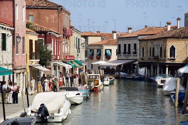 ITALY, Veneto, Venice, Tourists walking past shops along the Fondamenta dei Vetrai with boats moored on the Rio dei Vetrai canal on the lagoon island of Murano