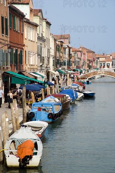 ITALY, Veneto, Venice, Tourists walking past shops along the Fondamenta dei Vetrai with boats moored on the Rio dei Vetrai canal on the lagoon island of Murano