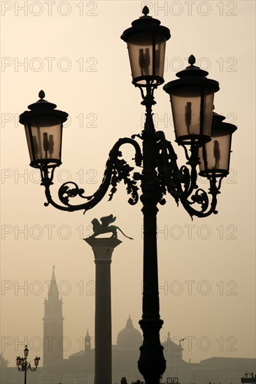 ITALY, Veneto, Venice, An ornate lamp post and the Column of Saint Mark in the Piazzetta with Palladio's church of San Giorgio Maggiore on the island of the same name in the distance on a misty day