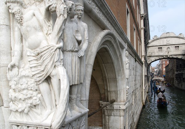 ITALY, Veneto, Venice, "A 15th Century stone carving depicting the Drunkenness of Noah, symbolic of the frailty of man, on the corner of the Doges Palace. Gondolas pass along the Rio Del Palazzo under the Bridge of Sighs "