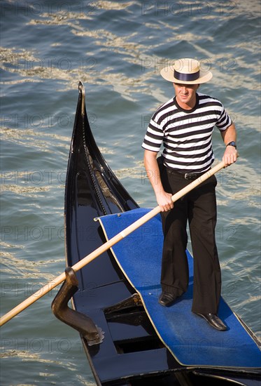 ITALY, Veneto, Venice, "A gondolier in traditional dress of beribboned straw hat, striped vest and black trousers on his gondola"