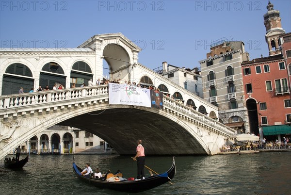 ITALY, Veneto, Venice, Gondolas carrying sightseeing tourists pass under the Rialto Bridge lined with people