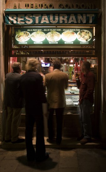 ITALY, Veneto, Venice, Men standing and eating at the street window of a restaurant near the Goldoni Theatre