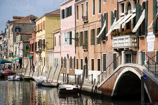 ITALY, Veneto, Venice, Colourful houses along the Fondamenta de la Sensa in Cannaregio district with boats moored along the canal and people walking along the pavement