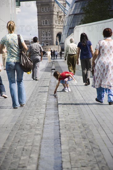 ENGLAND, London, People walking passed man made stream toward GLA town hall and Tower Bridge.