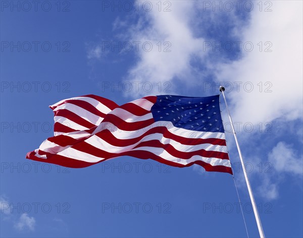 USA, Flags, American Stars and Stripes National Flag blowing in the wind against a blue sky with clouds