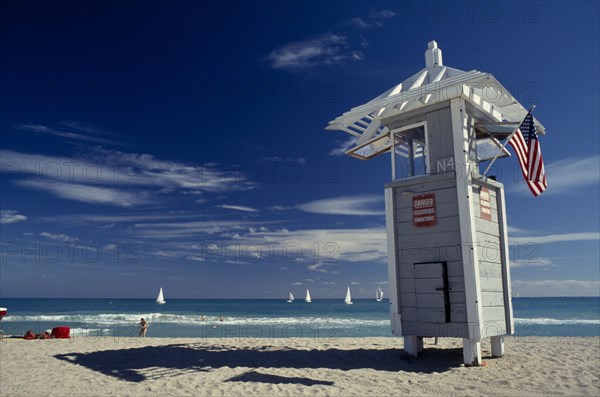 USA, Florida, Fort Lauderdale Beach, Lifeguard Tower displaying American flag with sailboats seen on turquoise sea behind