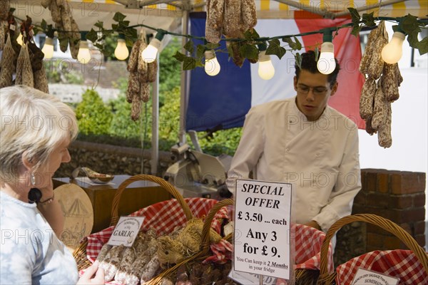 ENGLAND, West Sussex, Shoreham-by-Sea, French Market. Selection of sausages on display in baskets on stall with woman purchasing from male stall holder