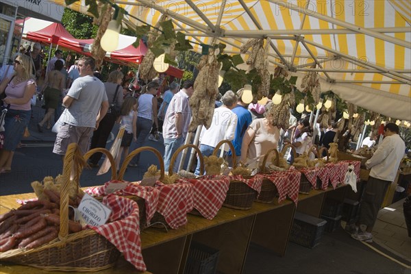 ENGLAND, West Sussex, Shoreham-by-Sea, French Market. Yellow and white striped covered market stall with a selection of sausages and cured meat on display.