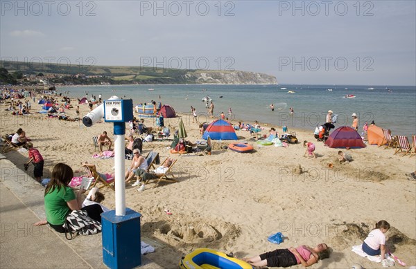 ENGLAND, Dorset, Swanage Bay, View across busy sandy beach with sunbathers on the sand towards the sea. Viewing telescope in the foreground.