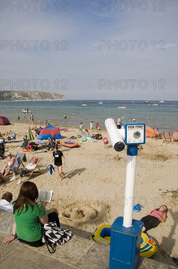 ENGLAND, Dorset, Swanage Bay, View over busy sandy beach with sunbathers on the sand towards the sea. Viewing telescope in the foreground.