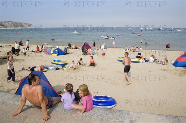 ENGLAND, Dorset, Swanage Bay, A man sat with small children looking out towards busy sandy beach with sunbathers on the sand and swimming in the sea