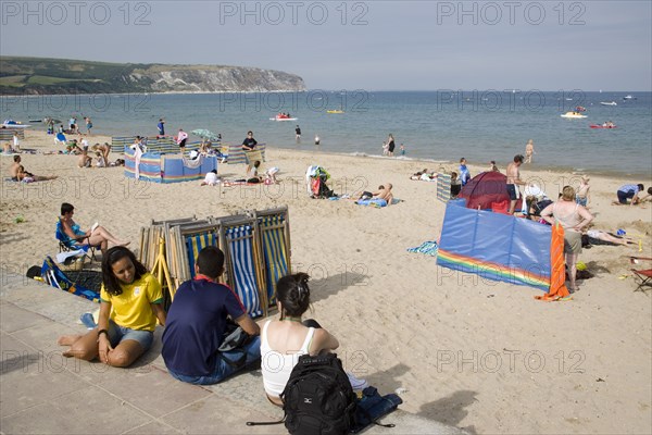 ENGLAND, Dorset, Swanage Bay, Busy sandy beach with sunbathers on the sand near deckchairs and windbreaks.