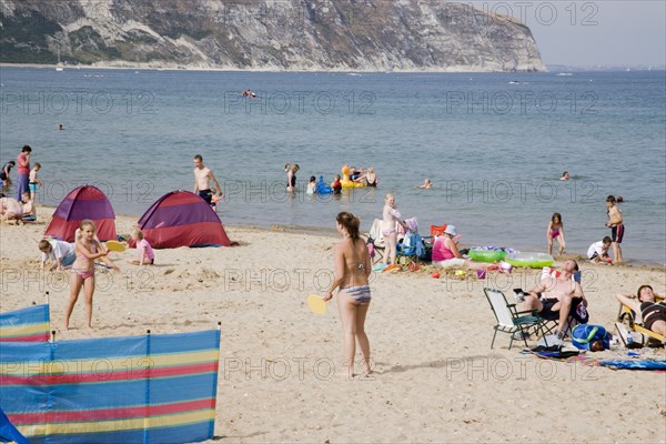 ENGLAND, Dorset, Swanage Bay, Sandy beach with girls playing Bat and Ball amongst sunbathers on sand and swimming in the sea